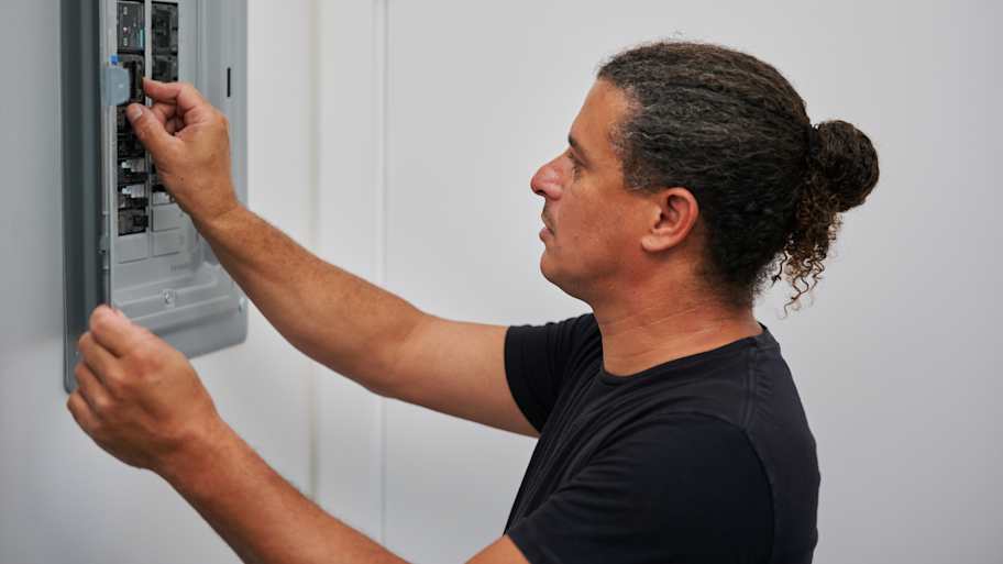 An electrician carefully inspects and adjusts circuit breakers in an electrical panel, focused on ensuring a safe and functional setup.
