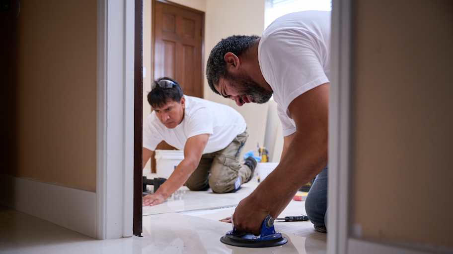 Two workers carefully position and adjust floor tiles with a suction tool, ensuring accurate alignment and a seamless finish.