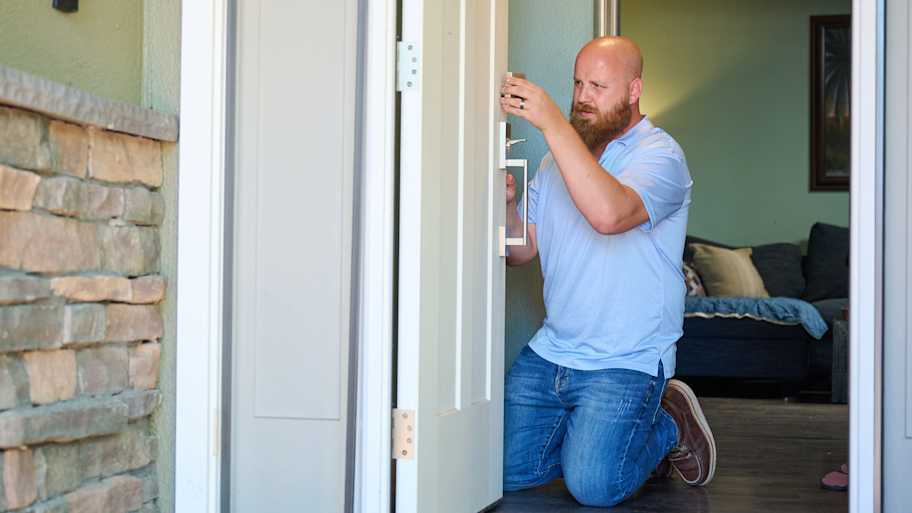 Handyman Chris McNeill from C.A. Shamrock LLC  installs a new door handle on an entry door, ensuring it aligns properly for smooth operation and security.