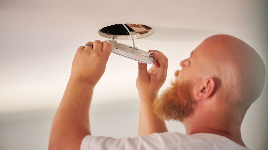 Handyman Chris McNeill from C.A. Shamrock LLC  carefully installs a ceiling light fixture, aligning the wiring to ensure a secure fit in the ceiling.