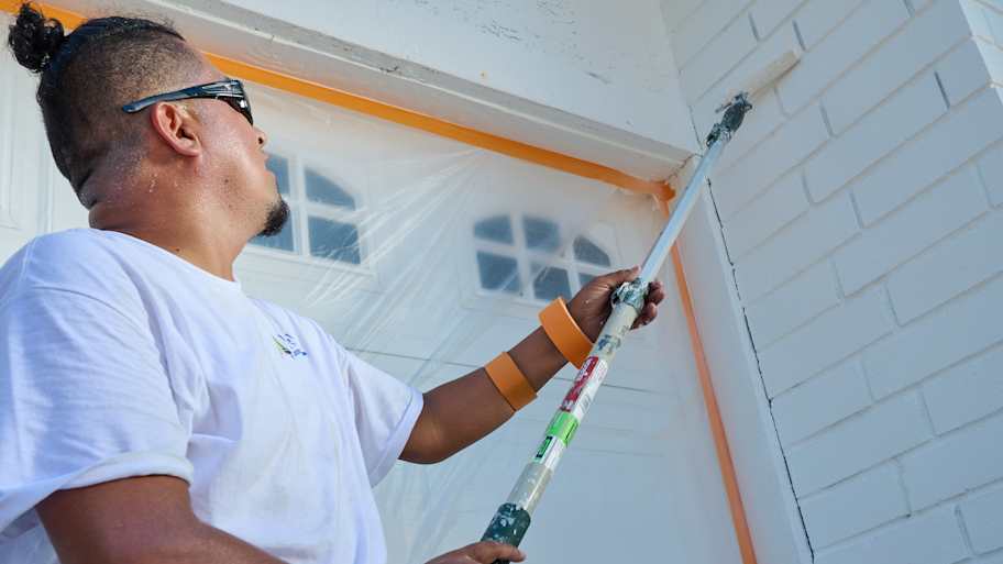 Man painting brick white near a garage door.