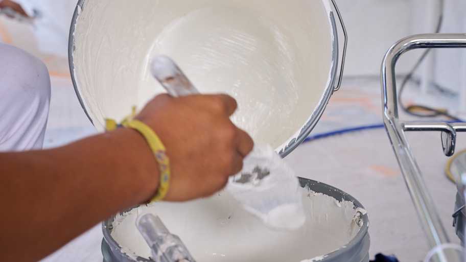Close-up of painter’s hand pouring white paint into a bucket, preparing for an exterior painting project.