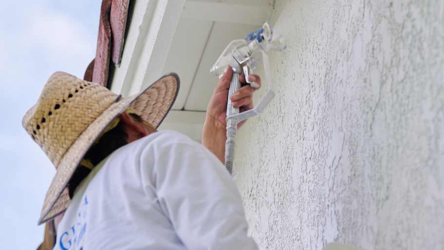 Painter carefully applies paint to a stucco wall, with fixtures covered and protective gear for a clean, safe application.