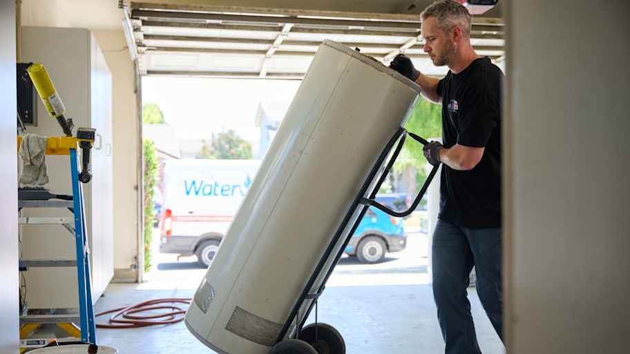 Technician carefully maneuvers a water heater on a dolly in a garage, preparing for installation or removal.