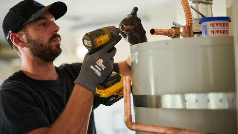 Technician using a power drill to install copper piping on a water heater, focused on precise fitting and secure connections.