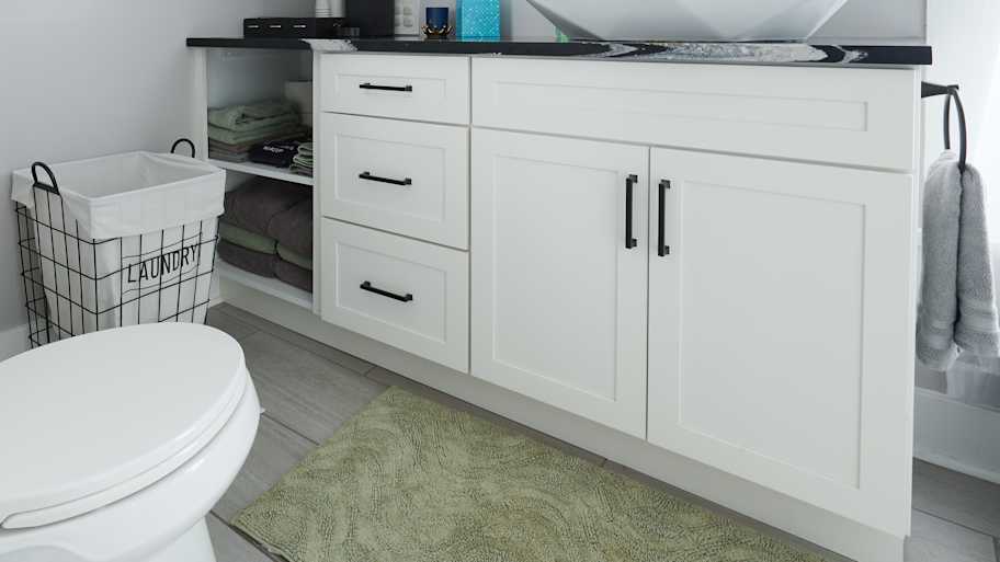 A modern bathroom with a sloped ceiling, featuring a white vanity, vessel sink, toilet, laundry basket, and sleek decor.