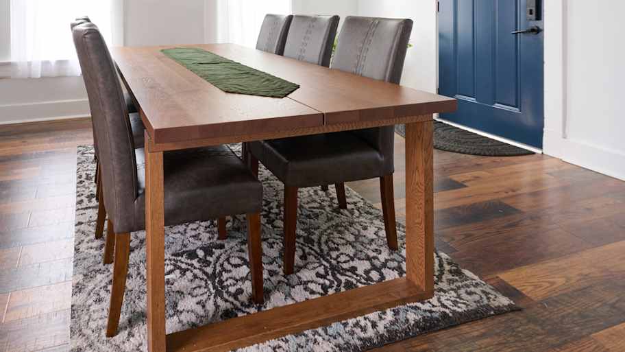 A bright dining room with a wooden table, six gray upholstered chairs, a blue door, and decorative wall art under a black chandelier.
