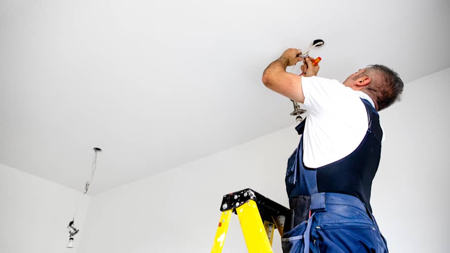 A repairman / a male electrician is fixing the light