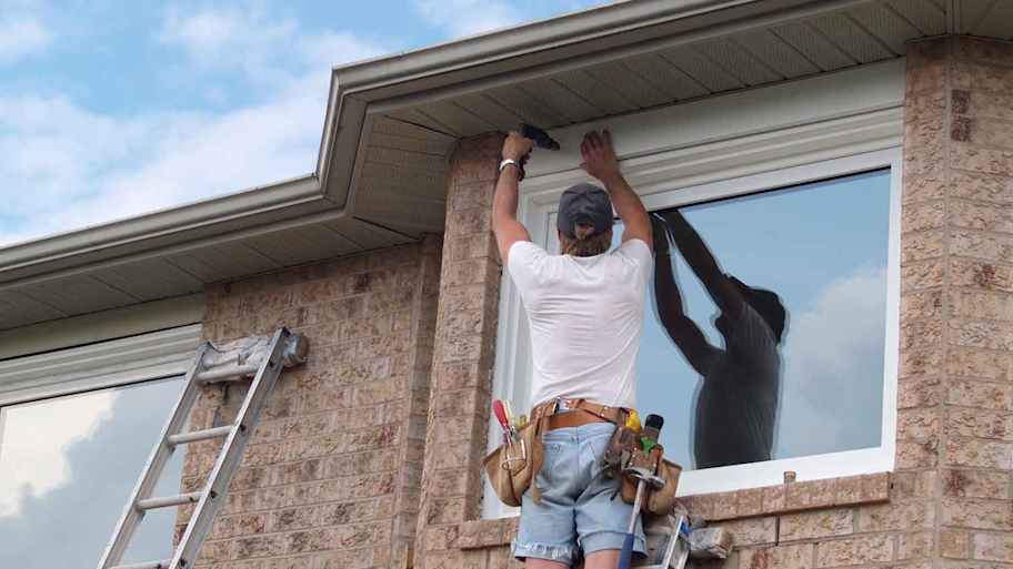 Handyman on a ladder drilling window trim
