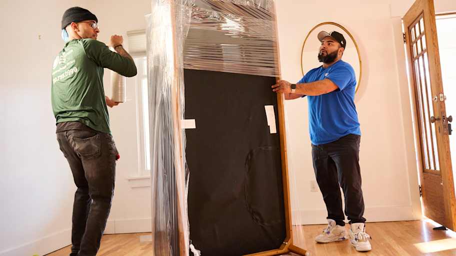 Two movers wrapping up furniture.