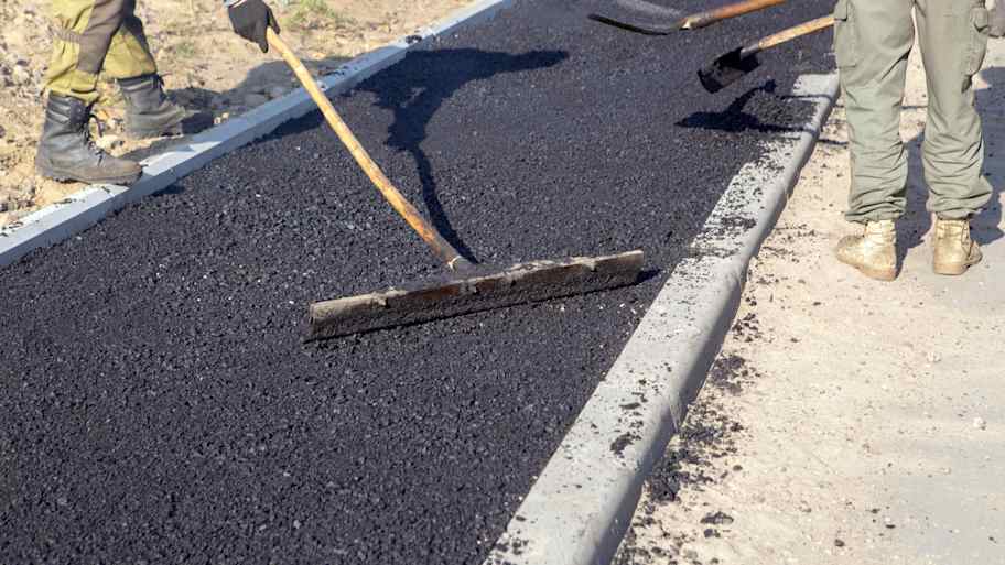 Workers use a squeegee tool to spread and level hot asphalt during an asphalt install, ensuring a smooth and even surface for the new pavement.
