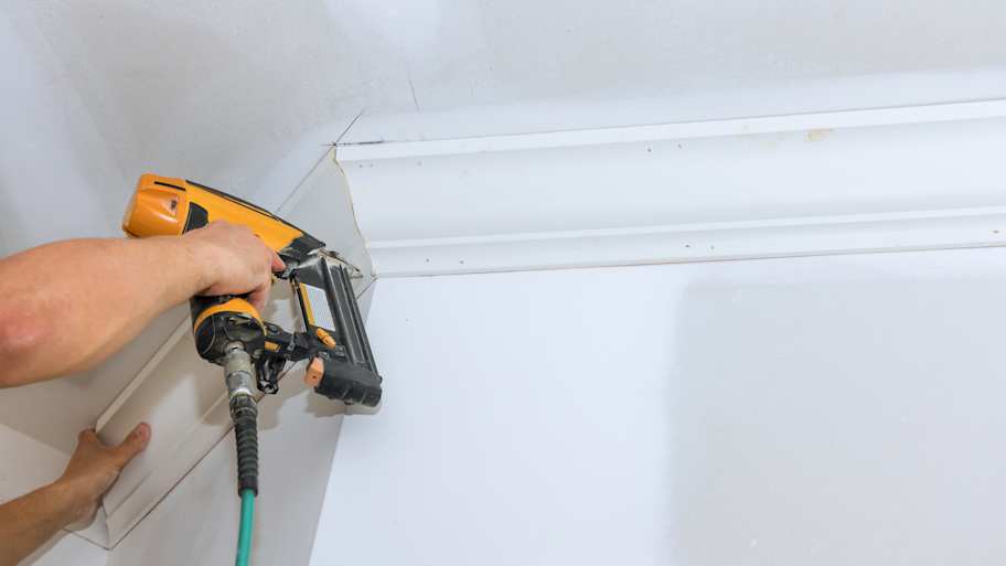 A person installing a crown molding with a nail gun 