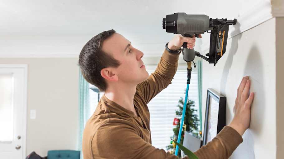 A man installing a crown molding using a nail gun 