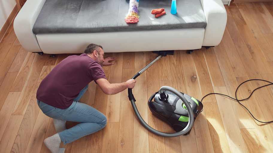 Man using a vacuum cleaner to clean under the sofa