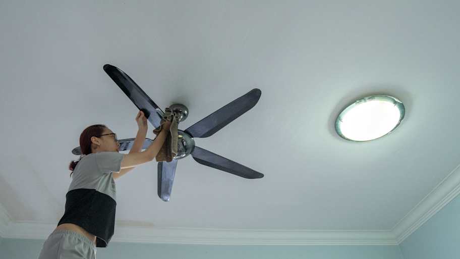 Woman using a cloth to clean a ceiling fan 