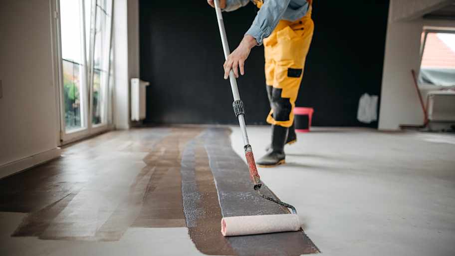Worker paints under the apartment with a roller.