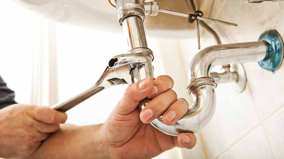 Plumber using a wrench to tighten a siphon under a sink
