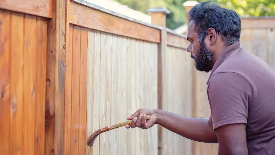 A man staining a fence with a brush
