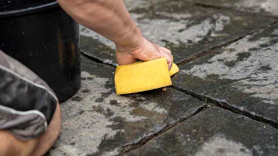 A person cleaning by hand pavers’ joints
