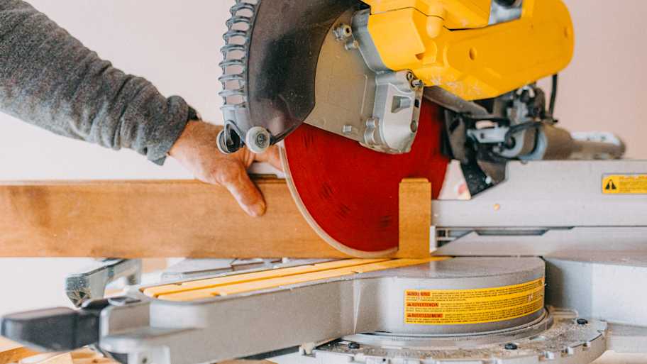 A man cutting a wooden baseboard with a miter saw