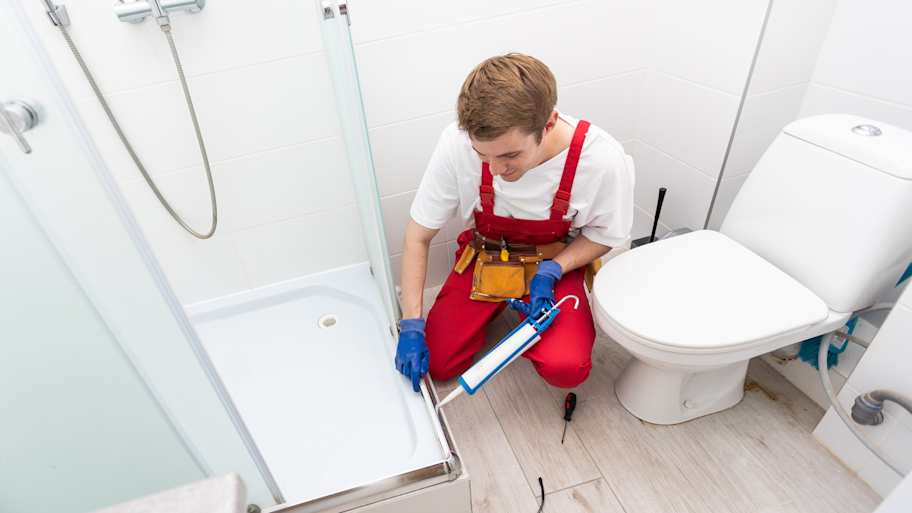Handyperson using waterproof silicone to seal a shower door 