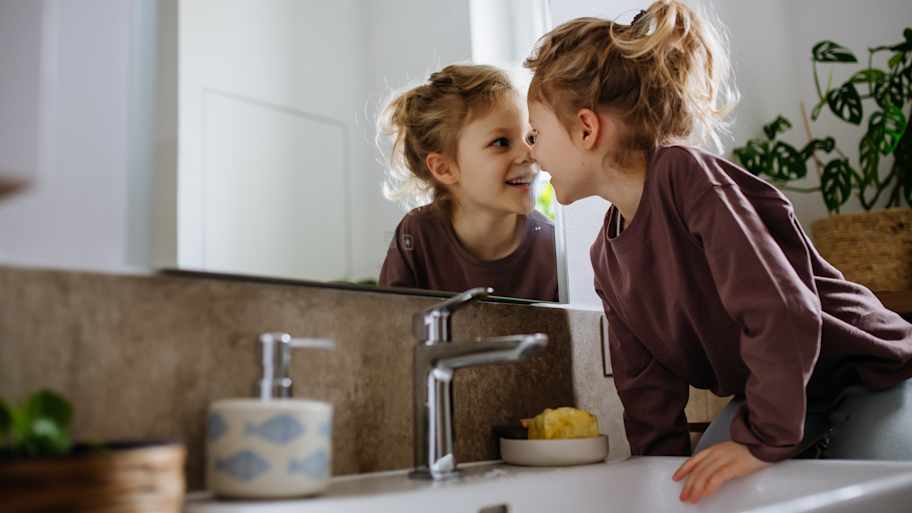 Little girl sitting in the bathroom, looking at her reflection