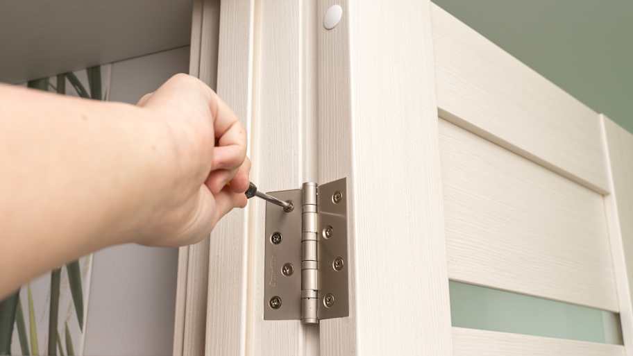 Person using a screwdriver to adjust a door hinge