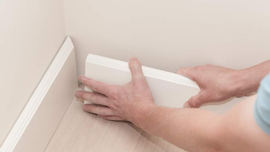 Person installing a white baseboard 