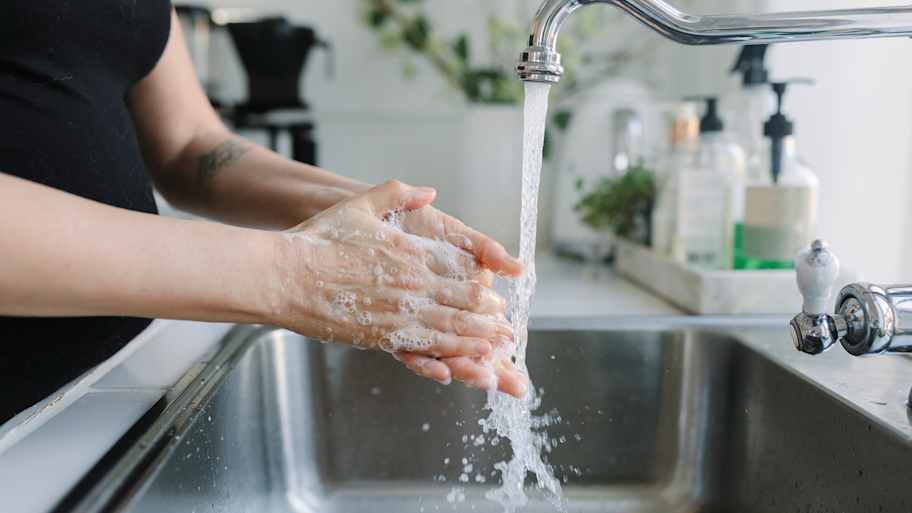 Woman washing her hands in a stainless-steel kitchen sink