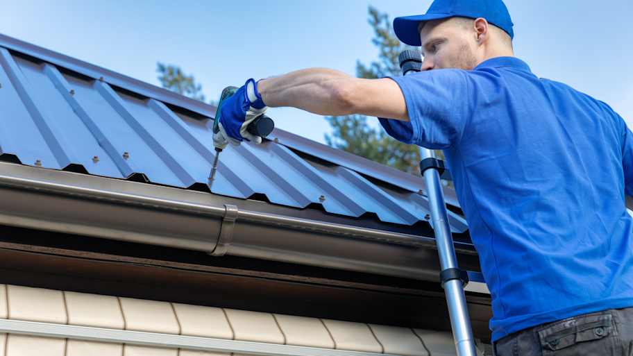 Roofer on a ladder installing a new metal roof on a house