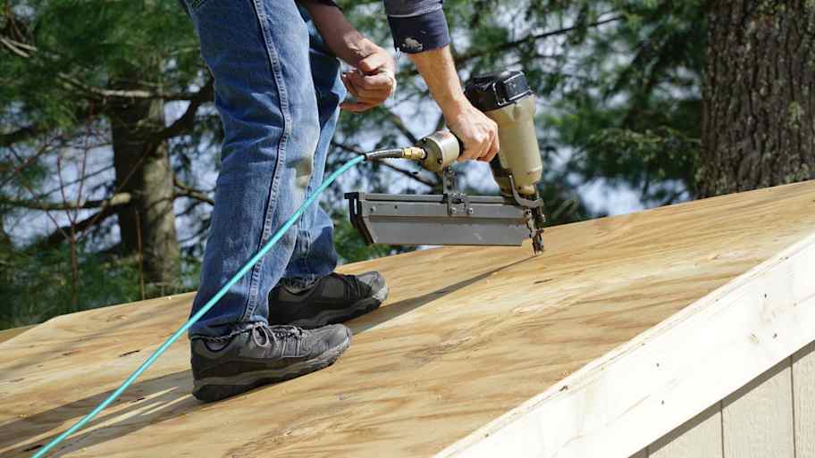 Contractor using a nail gun to attach wood panels to the roof   