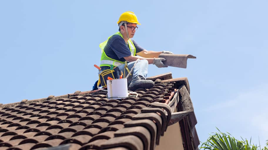 Roofer wearing safety gear repairing a tile roof