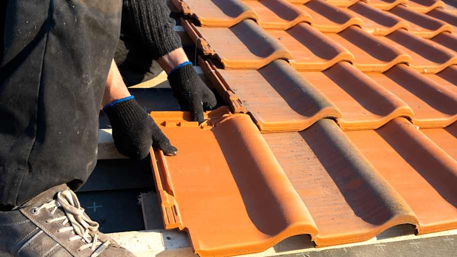 Worker installing new clay tiles on the roof