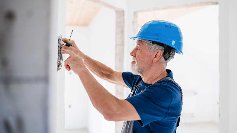 Senior man electrician with helmet working indoors on house construction site
