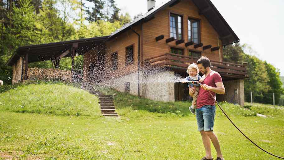 A man with his son watering the lawn in front of their home