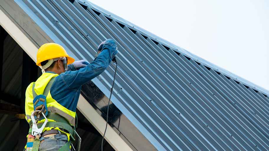 Worker wearing a safety harness repairing a metal roof   