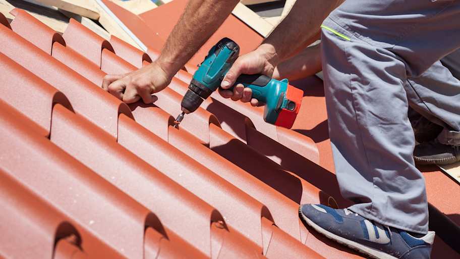 Worker attaching red metal tiles to the roof of a house  
