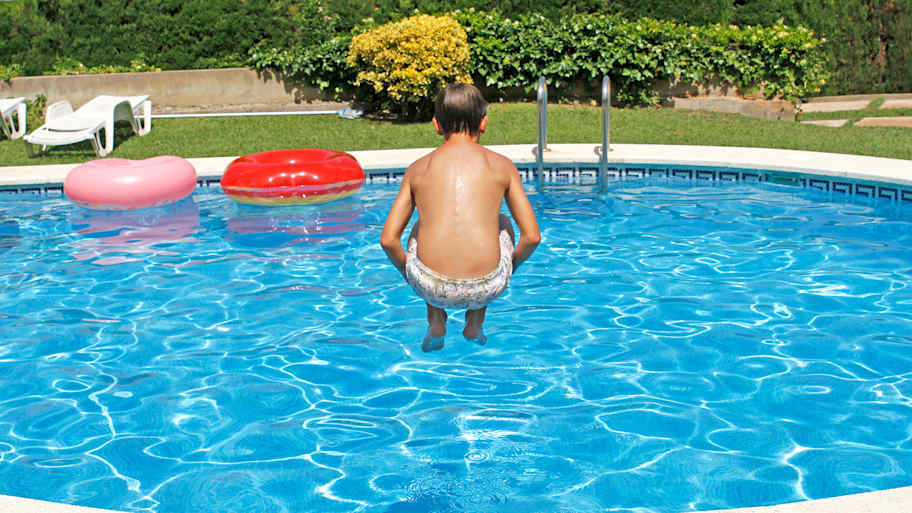 Boy jumping into an inground swimming pool