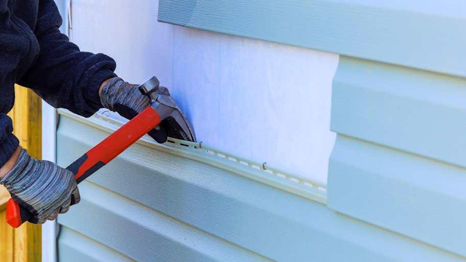Worker using a hammer to install vinyl siding