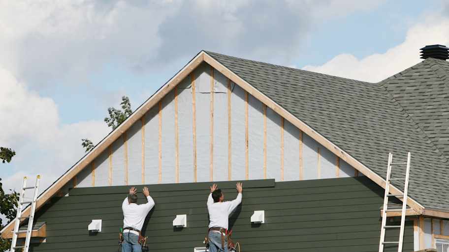 Two men installing green paneling to a house 