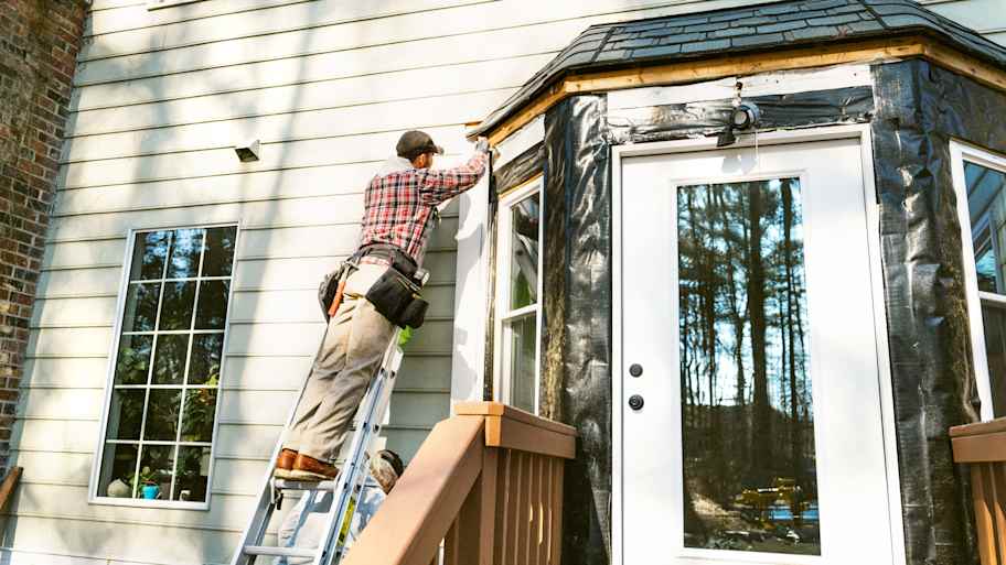 Worker on a ladder repairing wood siding 