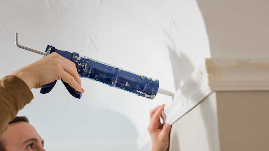 A person caulking a crown molding 