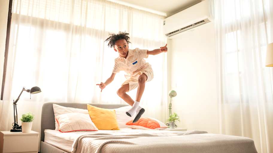Boy jumping on the bed in a bedroom with AC  
