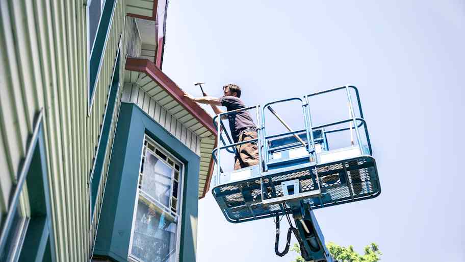 Roofer in a basket lift repairing the roof of a Victorian house