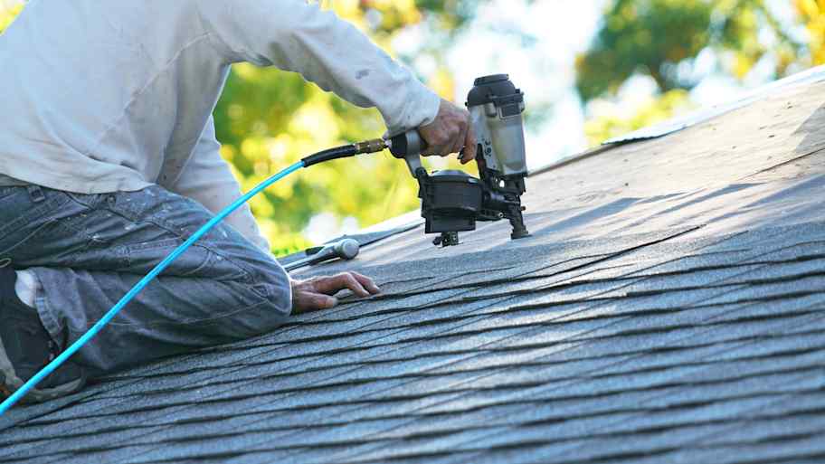 Worker using nail gun to attach asphalt shingles to the roof 