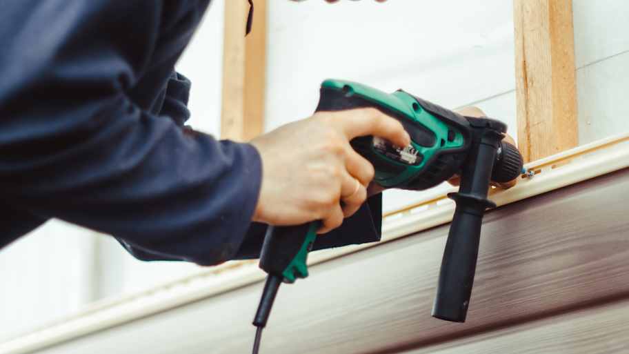 A worker installs panels beige siding on the facade of the house