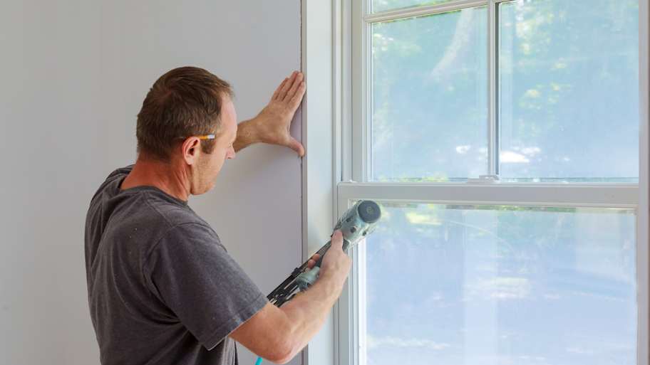 Worker using a nail gun to install a wood window trim