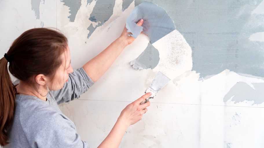 Woman using a scraper to remove wallpaper from the wall 