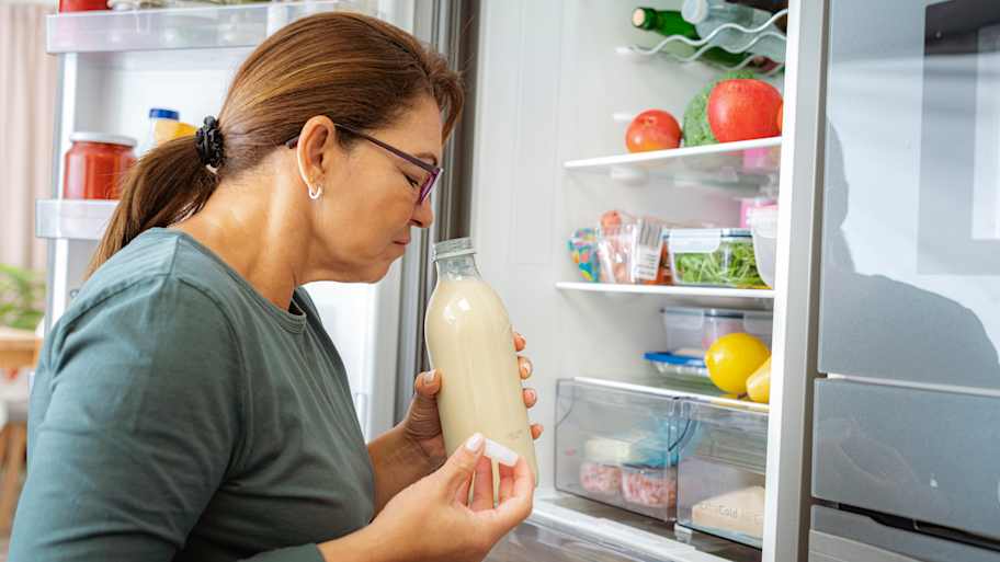 A senior woman smelling a milk bottle from the refrigerator