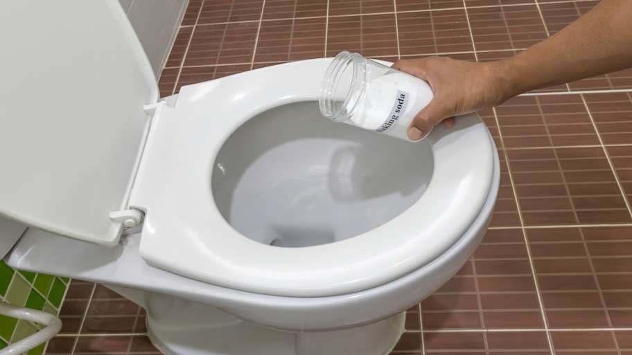 A person pouring baking soda on a toilet